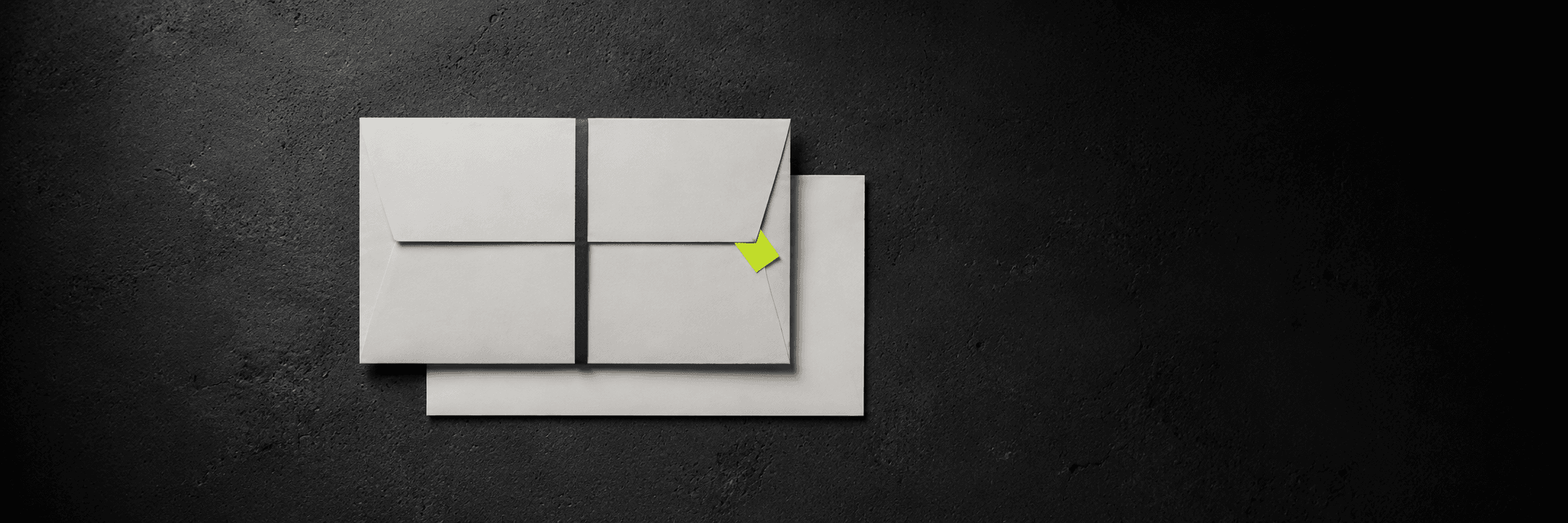 Sealed off-white envelope with a charcoal paper band and a small lime tag, on dark concrete