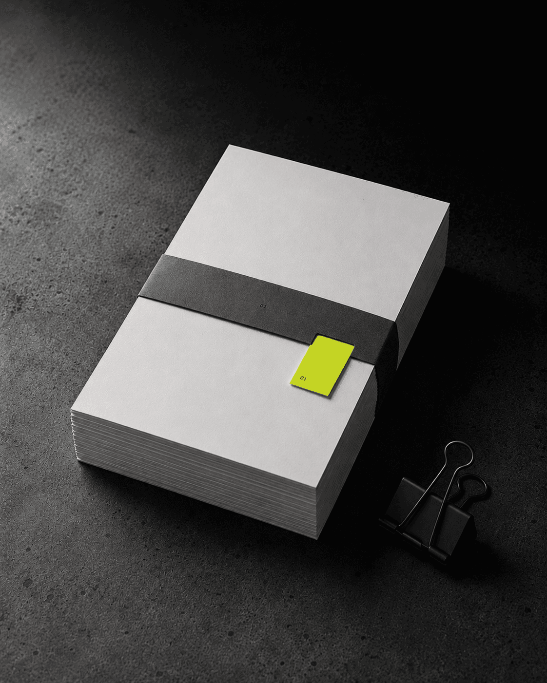 Bundle of plain cardstock sheets bound by a charcoal paper band on dark concrete